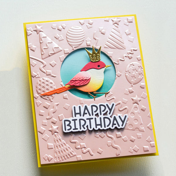 A handmade square birthday card with a pink embossed background, a yellow border, and a central circular cutout featuring a colorful bird wearing a gold crown above the words “HAPPY BIRTHDAY.”.