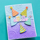 A handmade square birthday card with a white border, featuring embossed swirl patterns in a lavender-to-light-blue gradient background. The card displays five colorful, layered party hats and the words 'HAPPY BIRTHDAY' in pink letters.