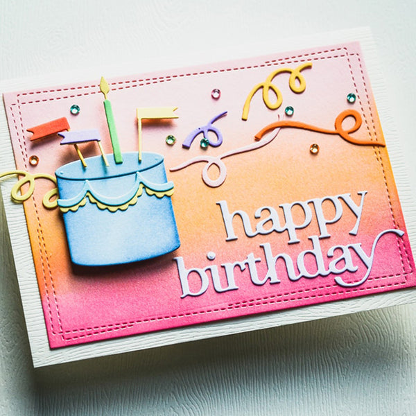 A handmade square birthday card featuring a colorful gradient background that fades from pink to orange to yellow. The card is decorated with a 3D blue birthday cake, lit candles, ribbon-like swirls, and the words 'happy birthday' in white script.