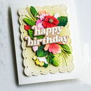 A handmade layered paper card with a scalloped cream border and a 3D floral design featuring the words 'happy birthday' in raised letters. The flowers and leaves are layered in shades of green, pink, red, and yellow on a white textured cardstock background.