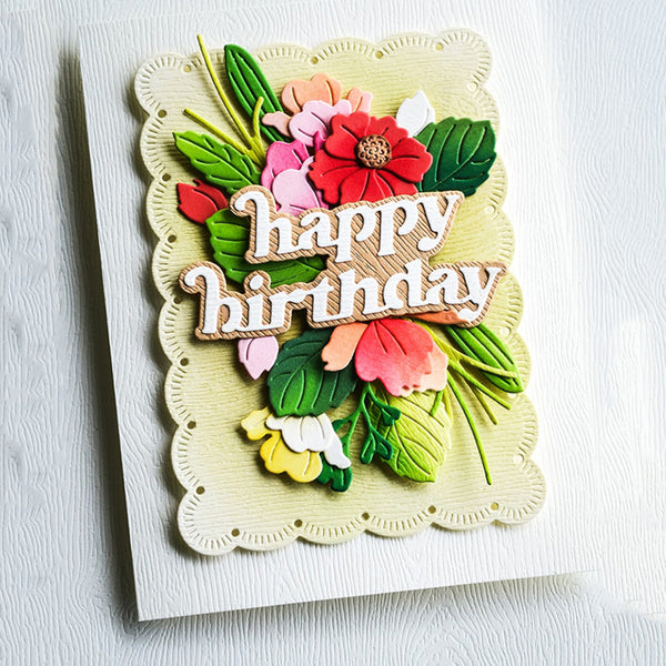 A handmade layered paper card with a scalloped cream border and a 3D floral design featuring the words 'happy birthday' in raised letters. The flowers and leaves are layered in shades of green, pink, red, and yellow on a white textured cardstock background.
