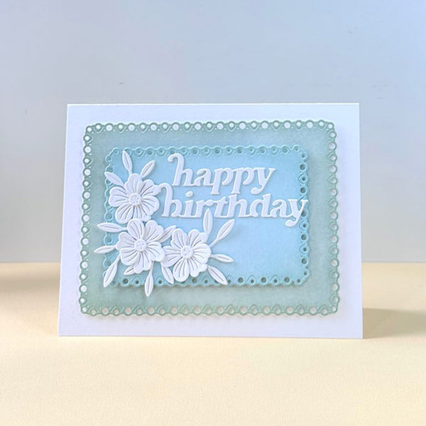 A handmade square birthday card with a white base, featuring a layered light blue and mint green scalloped frame, white floral cutouts, and the words 'happy birthday' in white script.