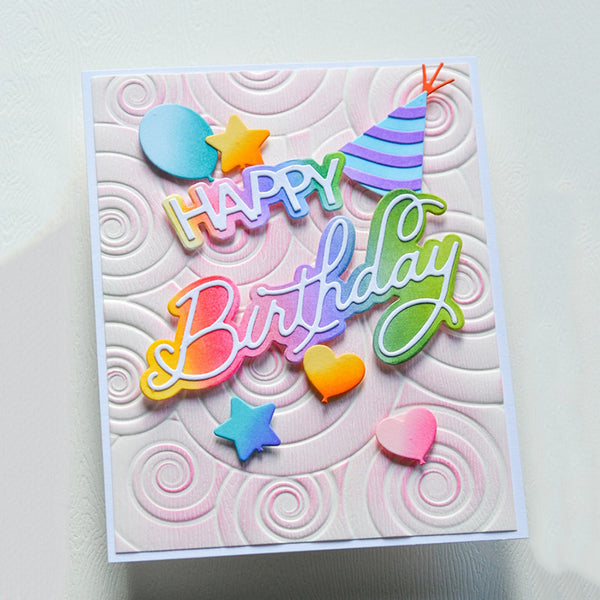 A square handmade birthday card with a white embossed swirl background and colorful layered lettering that reads 'Happy Birthday.' Decorative elements include pastel hearts, stars, and a striped party hat.