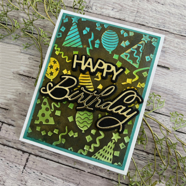 A handmade square birthday card with a green and black patterned background, featuring the words 'HAPPY Birthday' in layered black and gold glittery lettering. The card is styled on a rustic gray wooden surface with green sprigs.