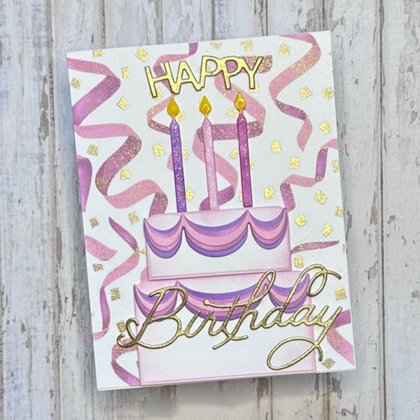 A handmade birthday card featuring a two-tiered cake with purple and pink striped layers, three lit purple candles, pink confetti streamers, and gold foil lettering that reads 'Happy Birthday'. The card is displayed on a light gray, weathered wood background.