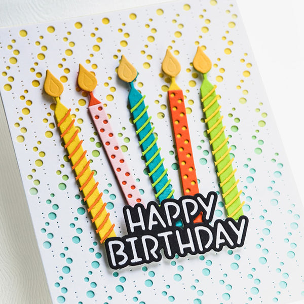 A close-up of a handmade birthday card featuring five colorful striped birthday candles with yellow flames and a black-and-white 'HAPPY BIRTHDAY' text overlay, set against a white card with a yellow and blue polka dot pattern.