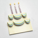 A two-tier birthday cake decoration set with pastel striped tiers and three glittery candle props on a light textured background.