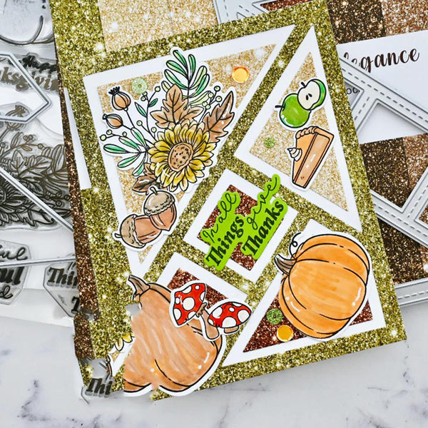 A handmade autumn-themed scrapbook card with a glittery gold border and multiple die-cut sections featuring pumpkins, acorns, a sunflower, a green apple, mushrooms, and the text 'have things and thanks'. The card is styled on a white marble surface with metal embosser sheets in the background.
