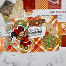 A styled flat-lay of craft cardstock sheets and glitter bags featuring autumn fall themes, including orange plaid, red and orange checkered patterns, and gold glitter. A Minnie Mouse sticker with the text 'Thankful Grateful Blessed' is placed on top of the cardstock.