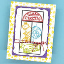 A handmade circus-themed greeting card featuring a white central panel with a purple border, yellow star-patterned outer border, and circus-themed line drawings including a ringmaster, lion, cannon, and a sign reading 'CIRCUS'. The card is tied with red-and-white twine and photographed on a light blue background.