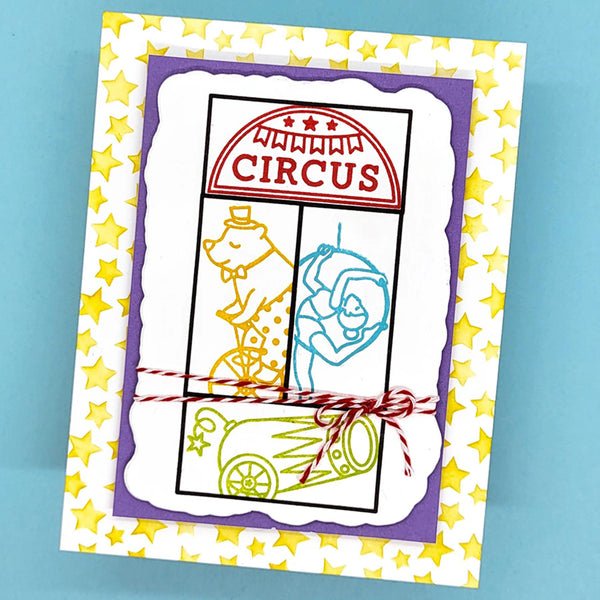 A handmade circus-themed greeting card featuring a white central panel with a purple border, yellow star-patterned outer border, and circus-themed line drawings including a ringmaster, lion, cannon, and a sign reading 'CIRCUS'. The card is tied with red-and-white twine and photographed on a light blue background.