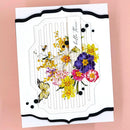 A handmade greeting card featuring a white embossed background with a central floral and butterfly illustration. The card has a black scalloped border and is photographed against a solid pink background.