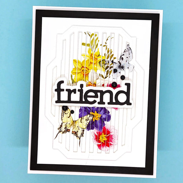 A handmade layered card featuring the word 'friend' in black script over a white background with butterfly and floral cutouts, set against a light blue backdrop.