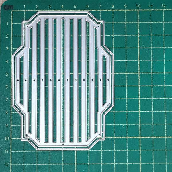 A clear acrylic or plastic die-cut template with a decorative border and vertical slat pattern, placed on a green cutting mat with grid lines and measurements.