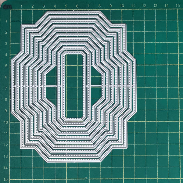 A set of nested metal die-cutting or stamping templates with an elongated oval and rectangular center cutout, arranged on a green cutting mat with grid lines.