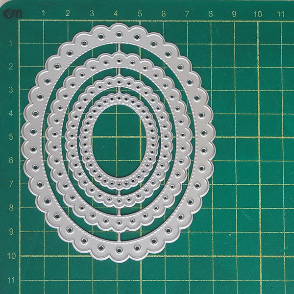 Three nested oval die-cut stencils with scalloped edges and small circular cutouts, displayed on a green gridded cutting mat.