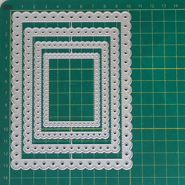 A set of five nested rectangular die-cut frames with scalloped edges and small circular cutouts, displayed on a green cutting mat with grid lines.