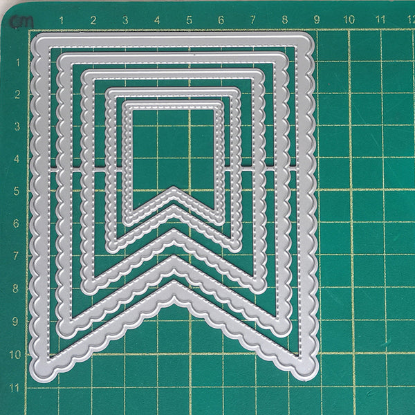 A set of silver metal embossing or stamping dies arranged in a nested chevron pattern on a green cutting mat with grid lines.