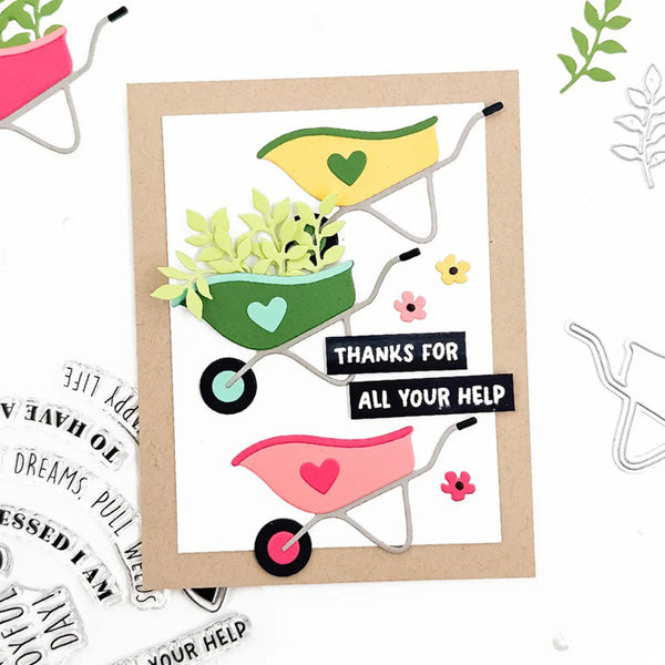 A handmade greeting card featuring three colorful hand-drawn wheelbarrows with green leaves and hearts, set on a white background with a kraft paper border. The center wheelbarrow has a black banner that reads 'THANKS FOR ALL YOUR HELP'.