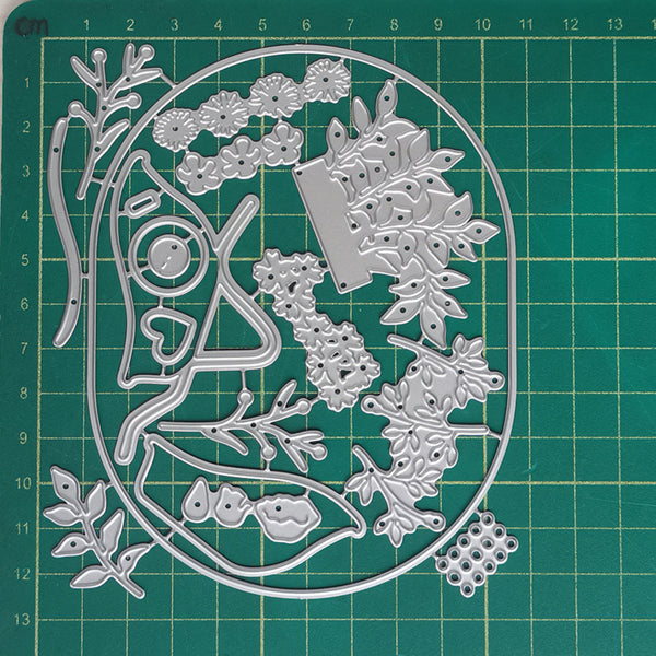 A metal die-cut craft sheet featuring a whimsical tree of life design with branches, leaves, acorns, and a heart-shaped trunk, displayed on a green cutting mat with grid lines.