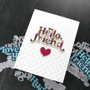 A handmade greeting card with 'Hello, friend' in multicolor bubble letters and a small pink heart, displayed on a dark wood background with metal die-cut lettering pieces.
