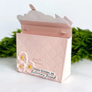 A handmade pink carded gift box with a quilted embossed pattern, decorated with 3D flowers and a script tag reading 'Happy Birthday, my luxurious friend'. The box is shown open, with green foliage in the background.