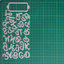 A clear plastic alphabet and decorative lettering mold set arranged on a green cutting mat with grid lines.