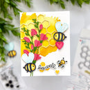 A handmade greeting card featuring a yellow honeycomb pattern, pink flowers, and cute cartoon bees with the word 'beewell' written in script. The card is displayed on a white surface with blurred green leaves in the background.