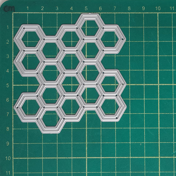 A silver metal hexagonal grid cutter or stencil template made of interlocking hexagons, placed on a green cutting mat with grid lines.