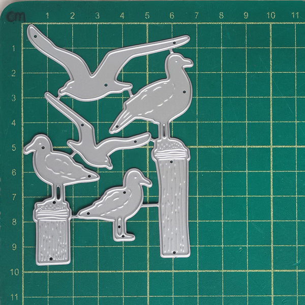 A set of six metal bird-shaped craft dies displayed on a green cutting mat with grid lines and centimeter measurements.