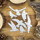 A set of bird-shaped metal cutting dies arranged on a rustic wooden surface with wood slices and pinecones around them.