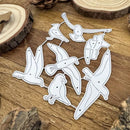 A set of white metal die-cut cutters shaped like birds, arranged on a rustic wooden surface with wood slices in the background.