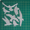 A set of silver metal bird-shaped craft dies or templates arranged on a green cutting mat with grid lines and measurement markings.