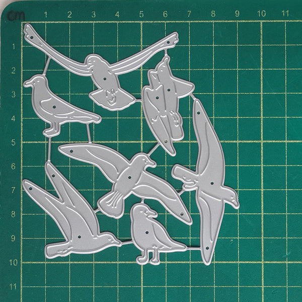 A set of silver metal bird-shaped craft dies or templates arranged on a green cutting mat with grid lines and measurement markings.