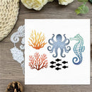 A white square card featuring ocean-themed designs: an orange and yellow coral cluster, a blue-gray octopus, a blue-green seahorse, black fish, and a white seahorse silhouette, displayed on a wooden surface with decorative flowers and woven matting.