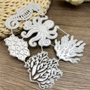 Silver metal die-cut craft embellishments featuring an octopus, seahorse, coral, and fish designs, arranged on a wooden surface with a woven straw prop.