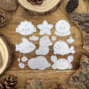 A set of nine white metal die-cut craft shapes featuring cute sea creatures like a starfish, octopus, fish, seahorse, whale, crab, and shell, arranged on a rustic wooden background with pine cones and wood slices.