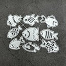 A set of nine silver metal fish-shaped die-cut pieces arranged on a dark textured gray background.