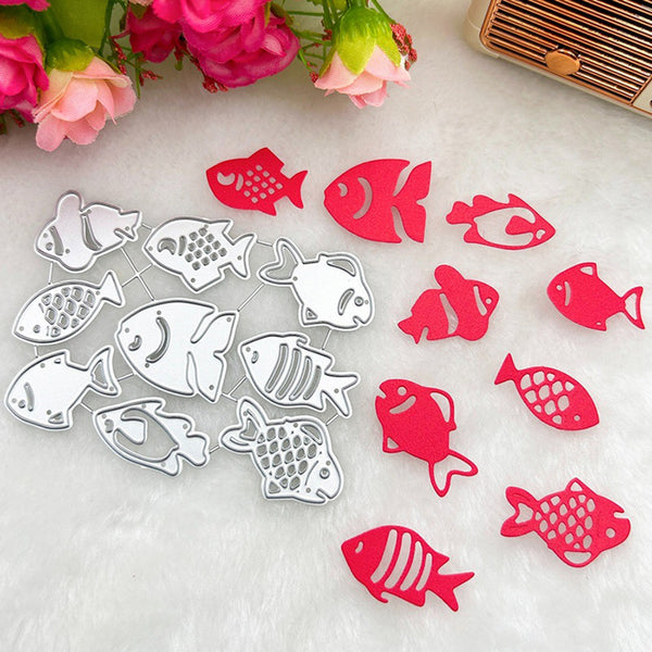 Fish-shaped metal cutters and matching red fish-shaped pieces arranged on a white textured surface with pink flowers and a small wooden object in the background.
