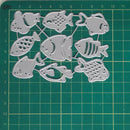 A set of silver metal fish-shaped craft dies arranged on a green cutting mat with grid measurements.