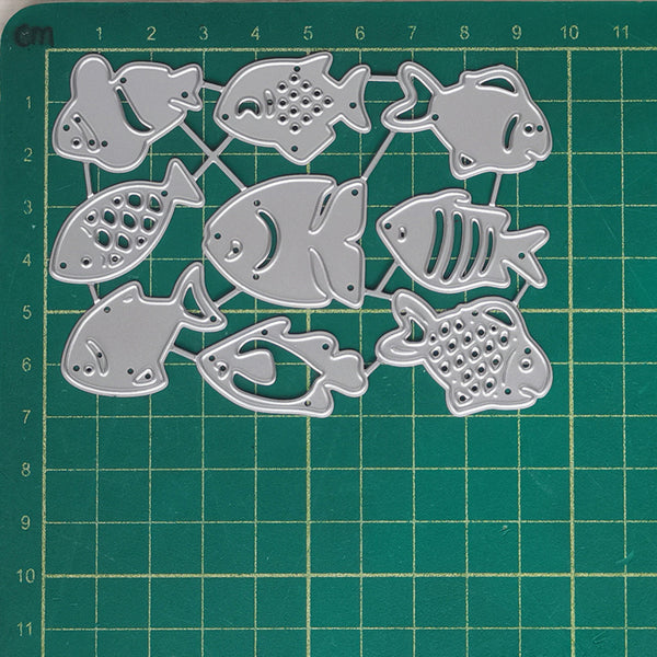 A set of silver metal fish-shaped craft dies arranged on a green cutting mat with grid measurements.
