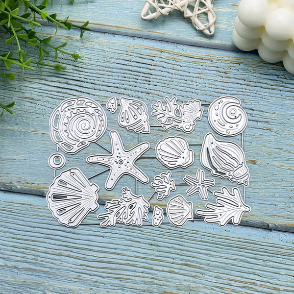 A set of metal seashell and starfish die-cut craft templates arranged on a light blue wooden surface with decorative seashells and greenery in the corners.