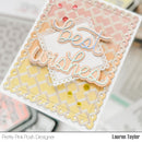 A close-up of a handmade greeting card with layered scalloped borders, pastel pink and yellow chevron patterns, and die-cut text reading 'Best wishes' in white with pale blue and peach outlines. The card is photographed on a blurred desk background, with 'Pretty Pink Posh Designer' and 'Lauren Taylor' printed at the bottom.