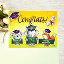A colorful congratulations card featuring cartoon animals wearing graduation caps and holding A-grade signs, displayed against a light brick wall with flowers on the left.