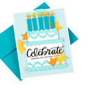 A handmade layered birthday card featuring a tiered cake with five blue candles, yellow glitter stars, and the text 'Celebrate Sending You Birthday Cheer', shown with a teal envelope on a white background.