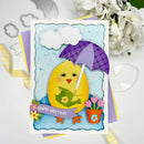A handmade layered greeting card featuring a yellow chick holding a green leaf under a purple plaid umbrella, with white clouds and pink flowers, displayed on top of other colorful cards and white flowers.