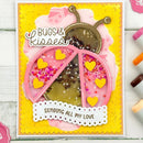 A handmade greeting card featuring a ladybug design made from clear plastic windows filled with glitter and small yellow heart embellishments, set against a bright yellow background with the words 'BUGS & KISSES' and 'SENDING ALL MY LOVE'.