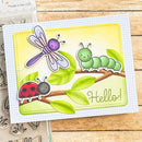 A handmade greeting card featuring cute cartoon bugs and leaves, displayed on a wooden surface next to a clear stamp sheet. The card has a white gingham border and a central yellow-green panel with a purple dragonfly, green caterpillar, red ladybug, and the word 'Hello!'.
