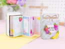 A decorative handmade gift box set displayed on a pastel surface. One box is open, showing pastel interior panels with fruit illustrations, and another closed box stands beside it with a lid decorated with a bow, fruit stickers, and the text 'JAM-PACKED with love.