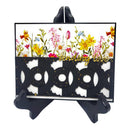 A decorative greeting card displayed on a black stand against a white background. The card features a white top section with a colorful watercolor-style floral design and the words 'sending love' in gold script, while the lower section is a black laser-cut geometric pattern with gold speckles.
